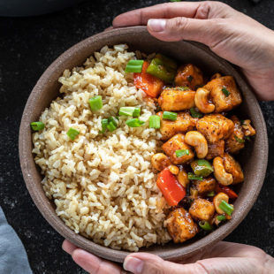 Paar Hände halten eine Schüssel Honig-Cashew-Tofu