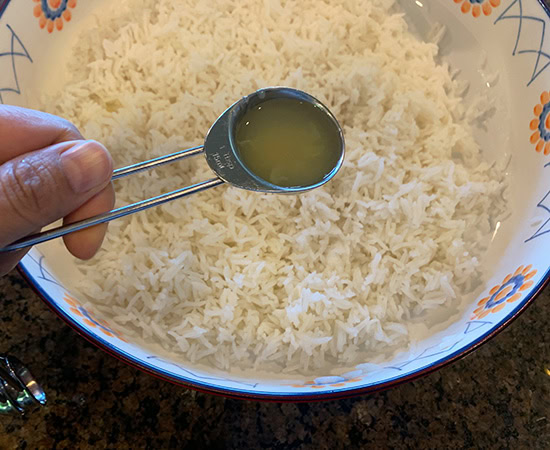 a hand adding teaspoon full of lemon juice to cooked rice