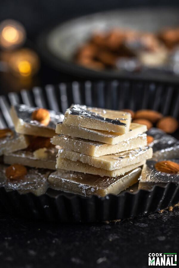 stack of badam burfi in a plate with some lights in the background