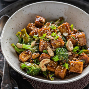 tofu broccoli roerbak geserveerd in een witte kom met een lepel aan de zijkant