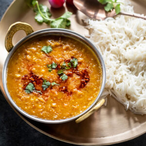 dal served in a copper kadai which is placed in a plate with boiled rice and pickled pearl onions served on the side