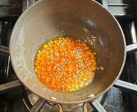 red chili powder added to a tadka in a small pan