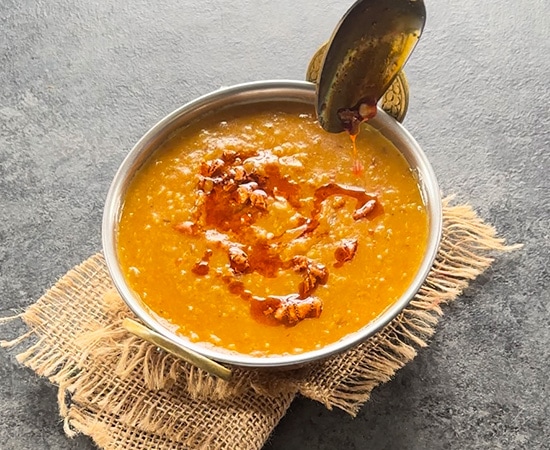 tadka being added to a dal served in a copper kadai with a spoon