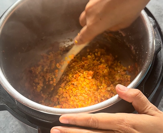 a wooden spatula stirring lentils in an instant pot