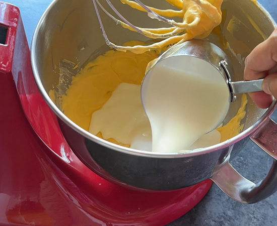a cup of heavy cream being added to a stand mixer