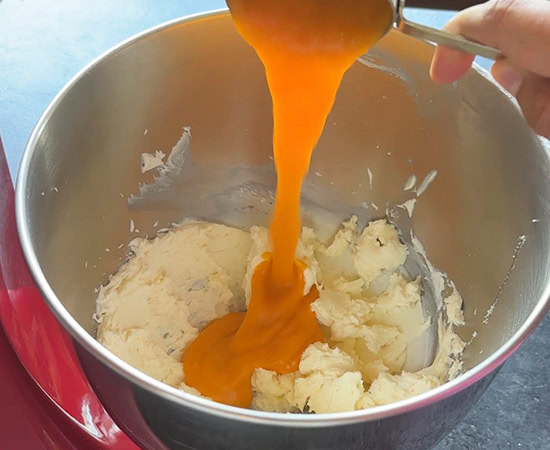 fresh mango puree being added to a stand mixer bowl with mascarpone cheese