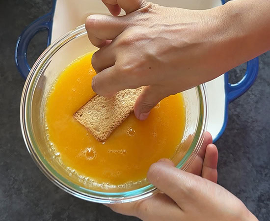 a hand dipping a rusk in mango puree mixture