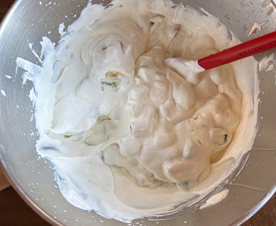 fruits folded into the whipped cream using a red spatula
