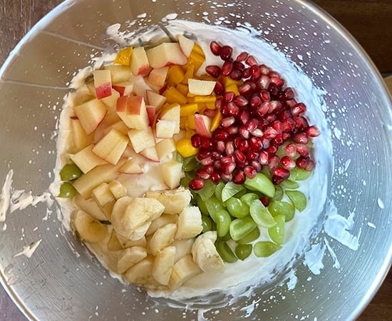 cut apples, grapes, banana, pomegranate seeds added to whipped cream