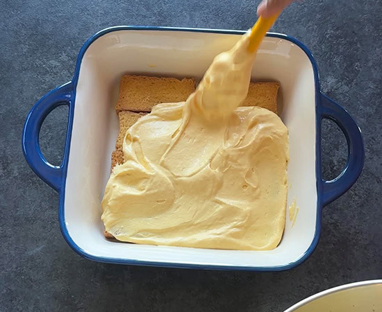 rusks being topped with mango puree mascorpone mixture using a spatula