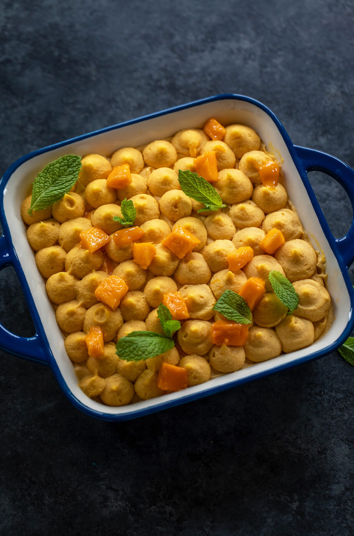 mango dessert in a square pan topped with mango pieces and mint leaves