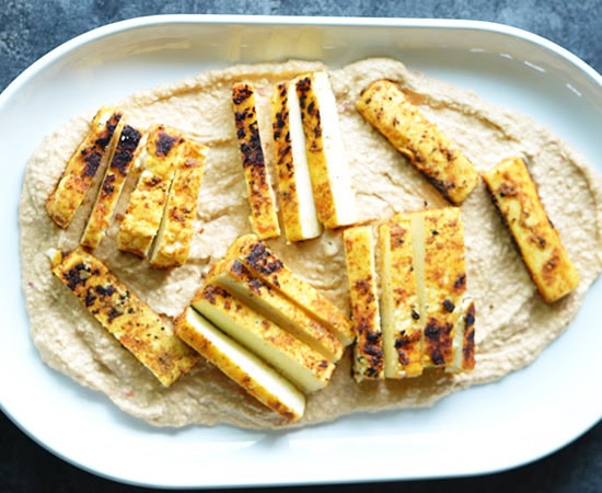 hummus topped with paneer strips on a white platter