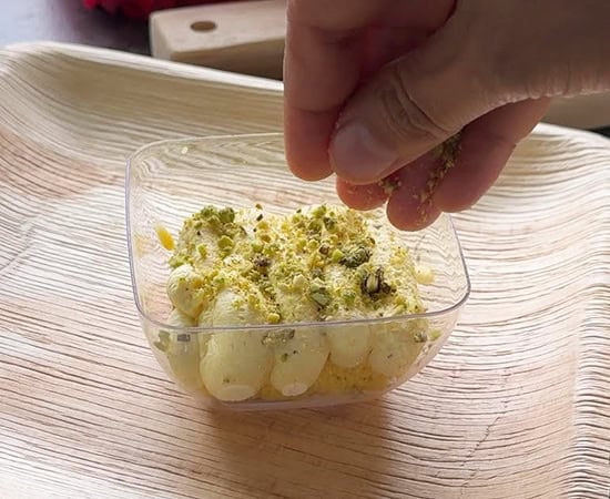 hand sprinkling chopped pistachios on top of mascarpone cheese