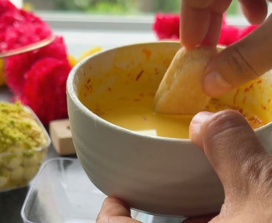 hand dipping ladyfinger cookie in saffron milk