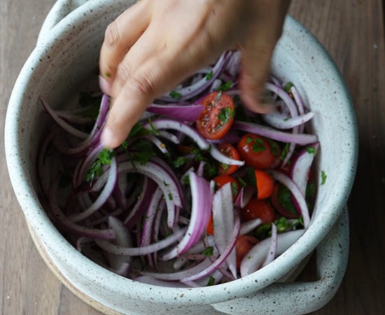 a hand mixing onions, tomatoes in a bowl