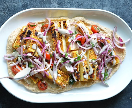 hummus topped with paneer, sliced onions, tomatoes and tahini sauce