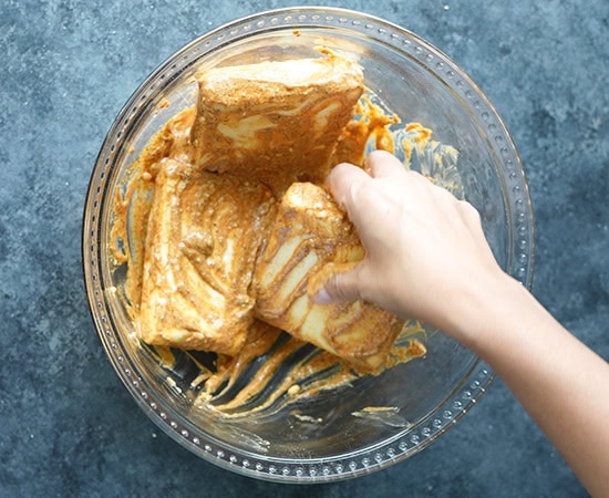 hand holding paneer slabs being coated in marinade