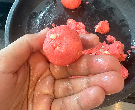 a hand holding a pink color ladoo