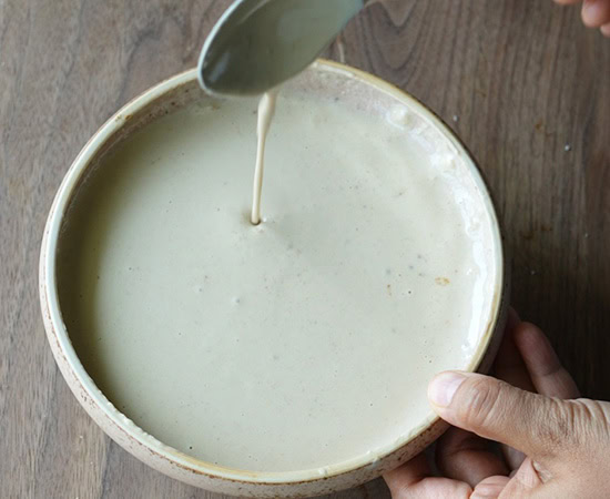 a spoon pouring tahini sauce to show its consistency