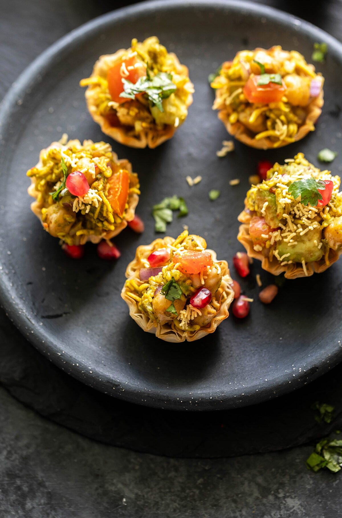 5 phyllo shells filled with chickpea, avocado arranged in a round black plate