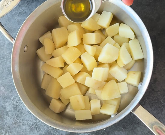 olive oil being added to cubed potatoes in a pan