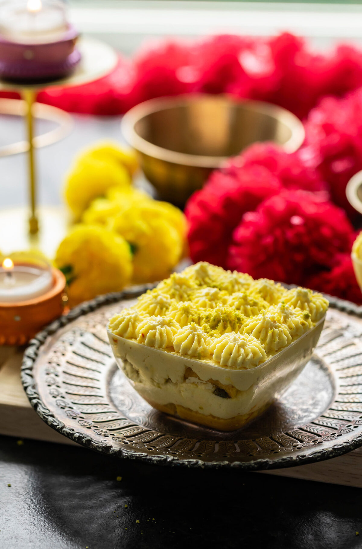 a dessert served in a square bowl with garlands of flowers and candles placed in the background