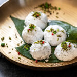 5 snowball cookies garnished with candied fennel place on betel leaves on a bronze plate