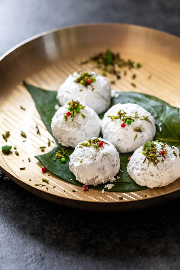 5 snowball cookies garnished with candied fennel place on betel leaves on a bronze plate