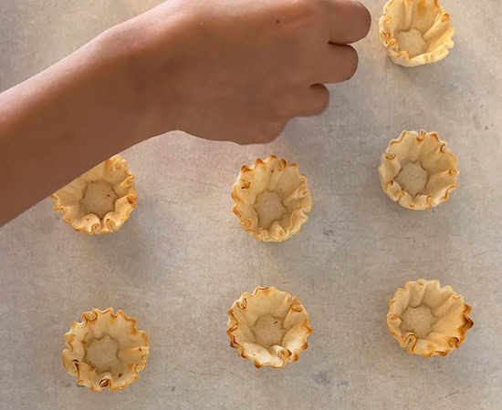 a hand arranging phyllo shells on a pan