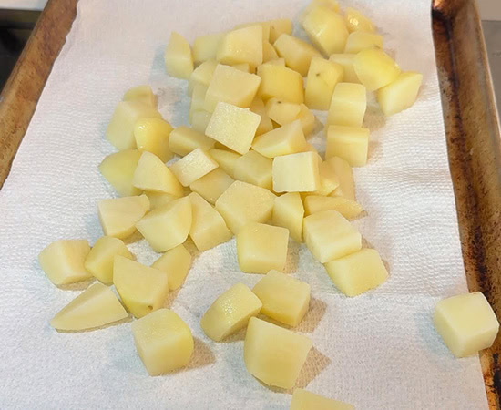 cubed potatoes placed on a baking sheet lined with paper towel