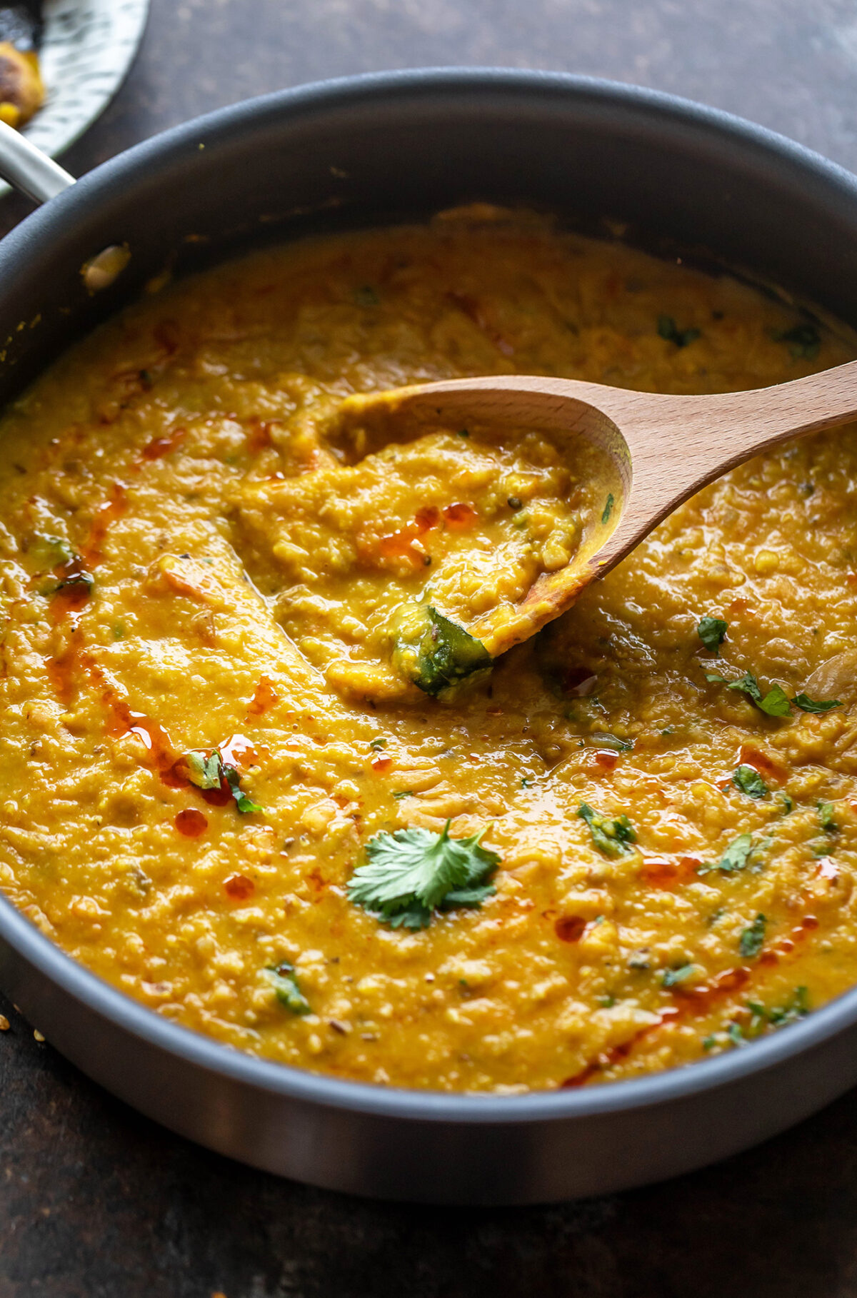 dal topped with cilantro in a pan with a wooden spatula place on the side