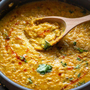 dal topped with cilantro in a pan with a wooden spatula place on the side